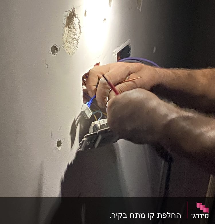 חשמלאי מחבר חוטים לשקע בקיר
